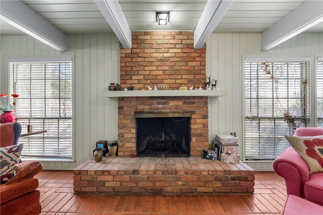 living room featuring a brick fireplace, beamed ceiling, and wood walls