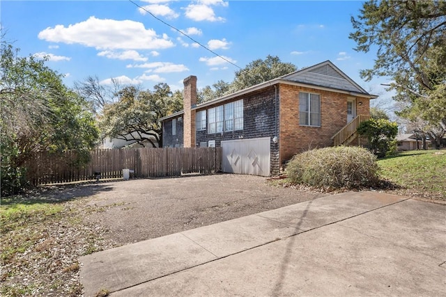 view of side of home with brick siding, an attached garage, driveway, and fence