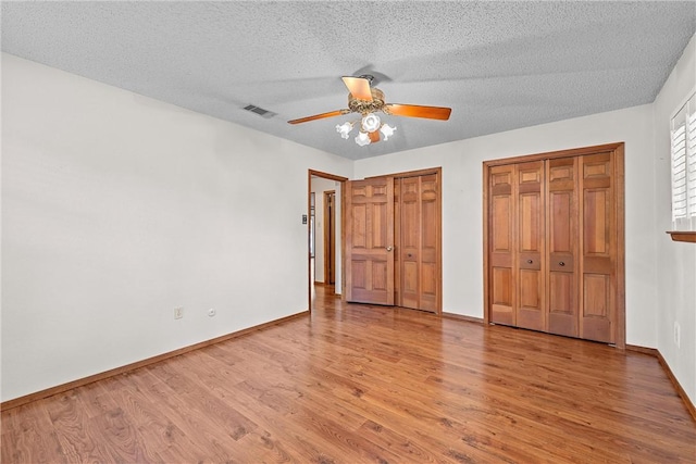 unfurnished bedroom featuring wood-type flooring, a textured ceiling, two closets, and ceiling fan