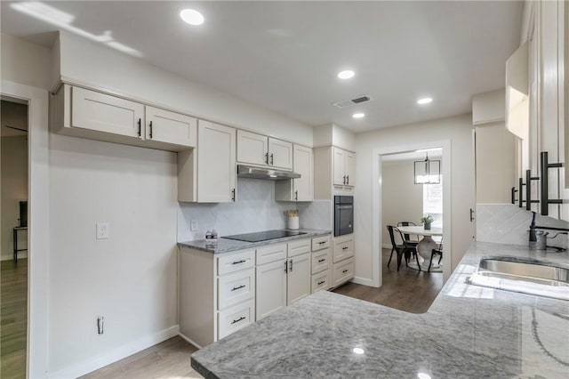 kitchen with tasteful backsplash, light stone counters, light hardwood / wood-style floors, white cabinets, and black appliances