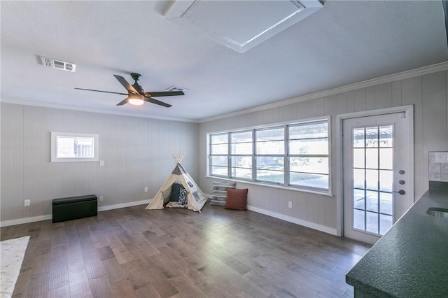 recreation room featuring wooden walls, crown molding, ceiling fan, and dark wood-type flooring