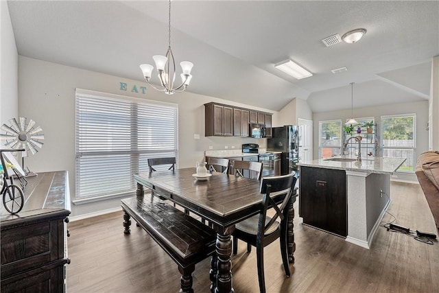 dining area with sink, wood-type flooring, lofted ceiling, and a notable chandelier