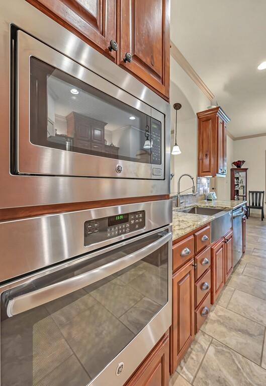 kitchen featuring hanging light fixtures, sink, ornamental molding, appliances with stainless steel finishes, and light stone counters