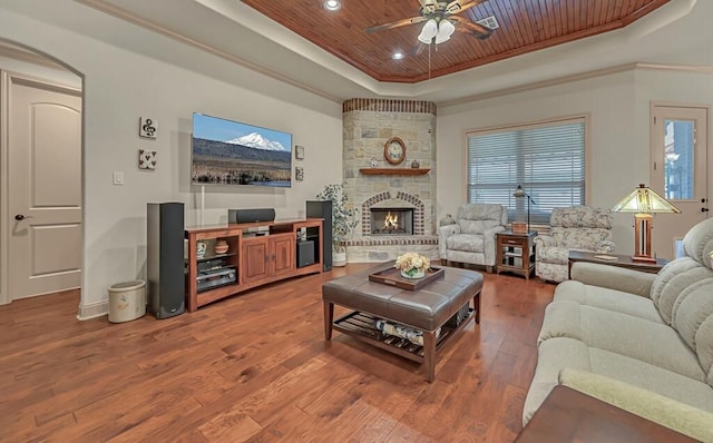 living room featuring a raised ceiling, ceiling fan, wood-type flooring, wooden ceiling, and a stone fireplace