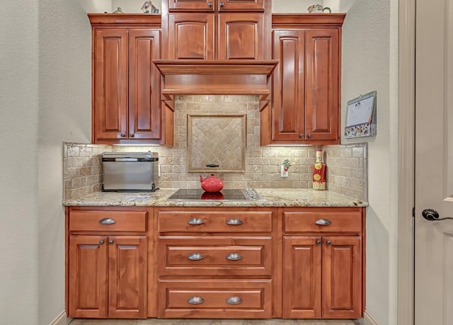 kitchen featuring black electric cooktop, decorative backsplash, and light stone countertops