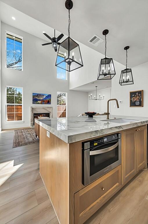 kitchen featuring stainless steel oven, sink, an island with sink, decorative light fixtures, and light stone counters