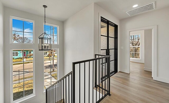 hall featuring light wood-type flooring, a healthy amount of sunlight, and a notable chandelier