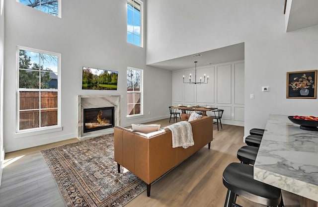 living room with a high ceiling, light wood-type flooring, a notable chandelier, and a premium fireplace