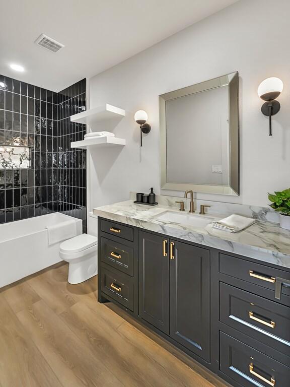 full bathroom featuring hardwood / wood-style floors, vanity, tiled shower / bath combo, and toilet