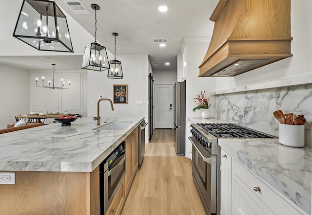 kitchen with custom exhaust hood, stainless steel appliances, sink, a barn door, and a center island with sink