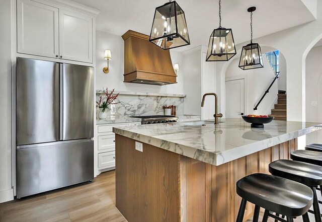 kitchen featuring white cabinetry, light stone countertops, stainless steel fridge, an island with sink, and light hardwood / wood-style floors