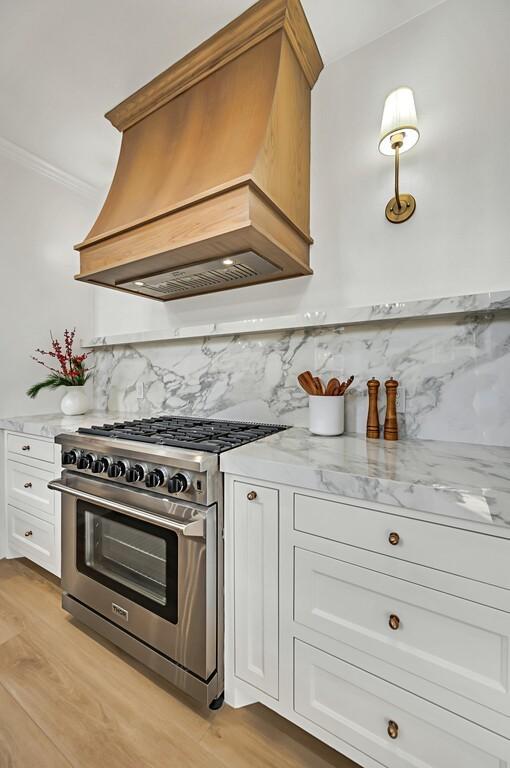 kitchen with premium range hood, white cabinets, stainless steel range, tasteful backsplash, and light hardwood / wood-style floors