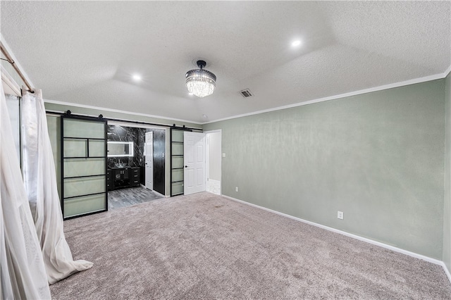 unfurnished bedroom with ornamental molding, a barn door, carpet flooring, and a textured ceiling