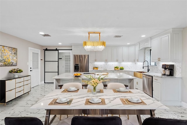 kitchen featuring pendant lighting, sink, appliances with stainless steel finishes, white cabinetry, and a barn door