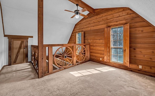 additional living space featuring light carpet, lofted ceiling with beams, ceiling fan, and wood walls