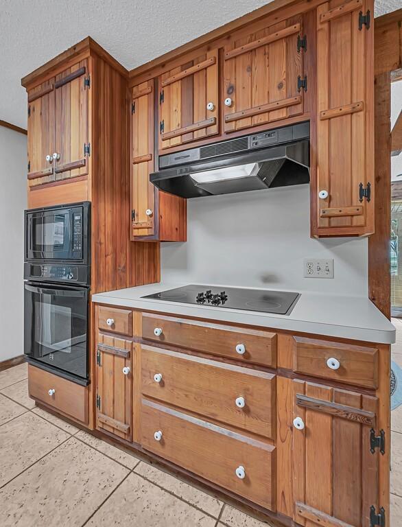 kitchen featuring light tile patterned floors, a textured ceiling, and black appliances