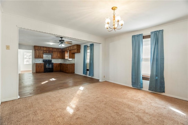 unfurnished living room featuring wood walls, sink, ceiling fan with notable chandelier, and hardwood / wood-style flooring