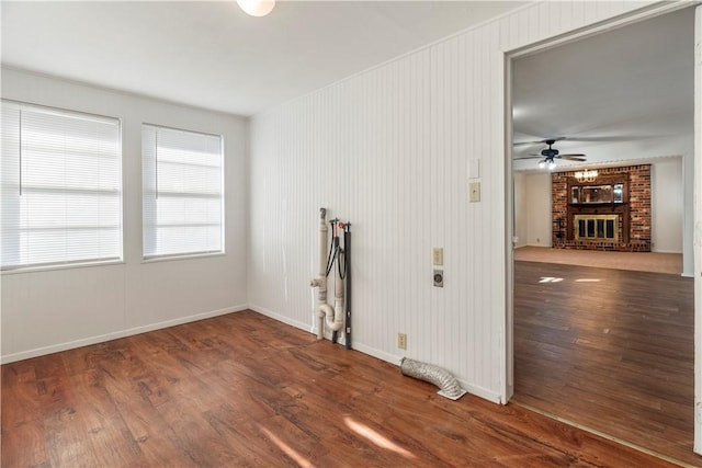 empty room featuring a fireplace, ceiling fan, and dark wood-type flooring