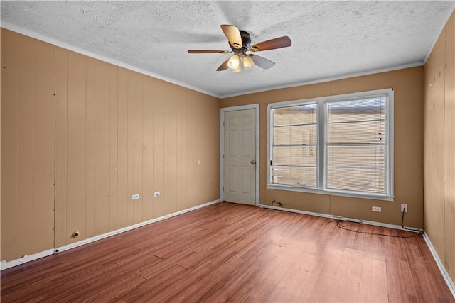 spare room with ceiling fan, a textured ceiling, wood finished floors, baseboards, and ornamental molding