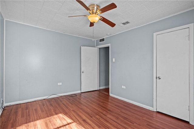 empty room with a ceiling fan, visible vents, crown molding, and wood finished floors