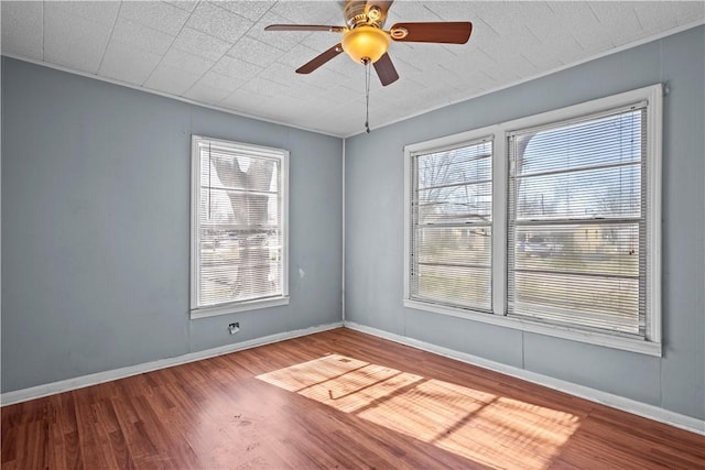 empty room featuring ceiling fan, plenty of natural light, wood finished floors, and baseboards