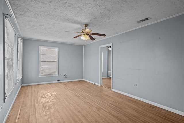 spare room with a textured ceiling, visible vents, light wood-style floors, baseboards, and crown molding