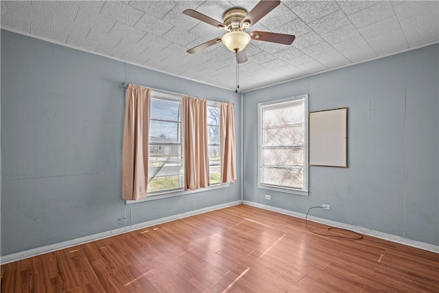 unfurnished room featuring a ceiling fan, light wood-type flooring, a healthy amount of sunlight, and baseboards