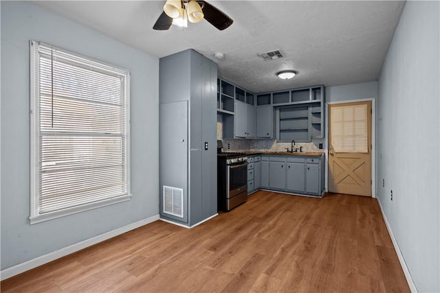 kitchen featuring visible vents, dark countertops, gray cabinets, open shelves, and stainless steel range with gas stovetop