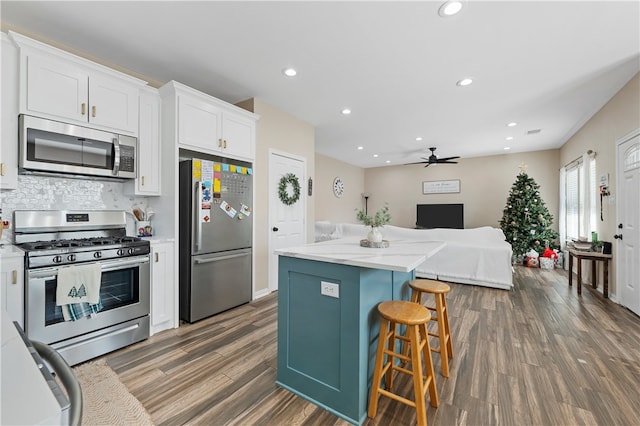 kitchen featuring ceiling fan, appliances with stainless steel finishes, a kitchen island, dark hardwood / wood-style flooring, and white cabinetry