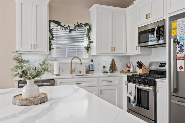 kitchen with backsplash, sink, light stone countertops, appliances with stainless steel finishes, and white cabinetry