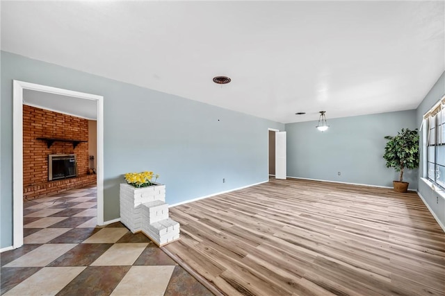 unfurnished room featuring a brick fireplace, baseboards, and wood finished floors