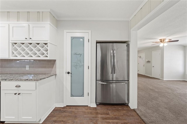 kitchen with white cabinets, decorative backsplash, light stone counters, ornamental molding, and freestanding refrigerator