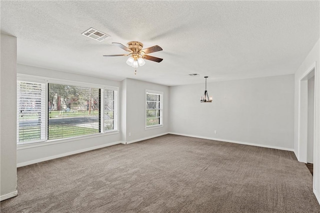 carpeted empty room featuring ceiling fan with notable chandelier, visible vents, and baseboards