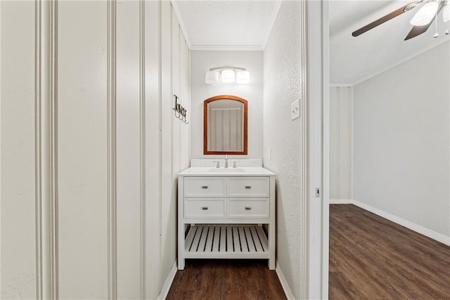 corridor with dark wood-style floors, a textured wall, a sink, and baseboards