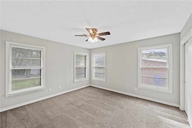 carpeted empty room with ceiling fan and baseboards