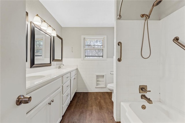 bathroom featuring double vanity, tile walls, toilet, wood finished floors, and a sink