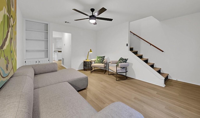 living room with built in features, visible vents, stairway, a ceiling fan, and wood finished floors