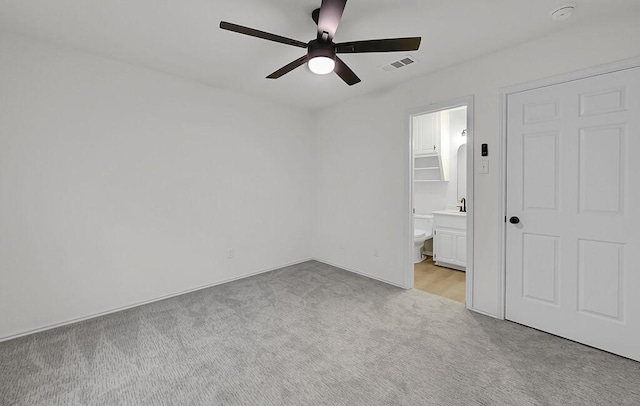 unfurnished bedroom featuring light colored carpet, ceiling fan, visible vents, and ensuite bath