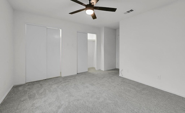 unfurnished bedroom with carpet floors, a ceiling fan, visible vents, and multiple closets