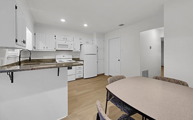 kitchen with white appliances, visible vents, white cabinets, a breakfast bar area, and light wood-style floors