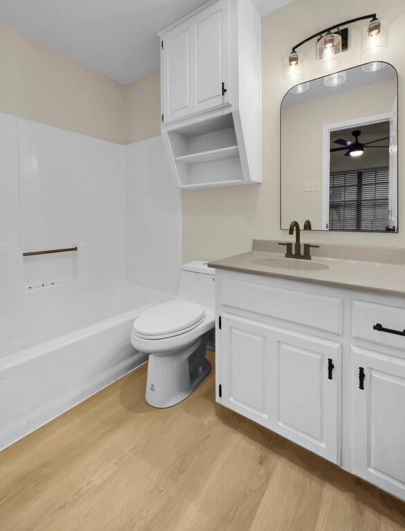 bathroom with toilet, shower / bathing tub combination, wood finished floors, and vanity