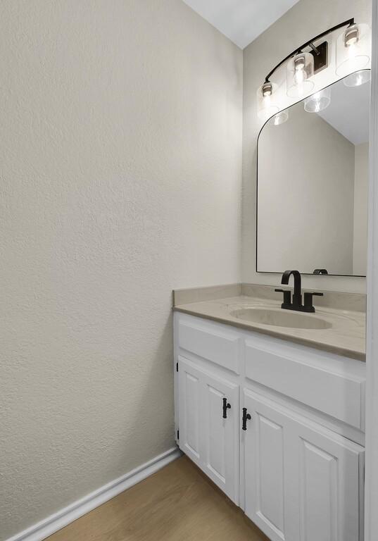 bathroom featuring a textured wall, vanity, baseboards, and wood finished floors