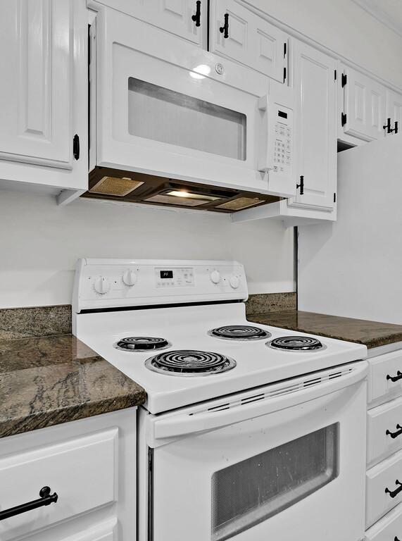 kitchen with white appliances, dark stone countertops, and white cabinetry