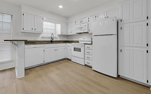 kitchen with dark countertops, light wood-style flooring, white cabinetry, a sink, and white appliances