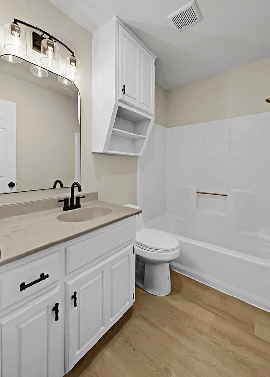 full bathroom with visible vents, toilet, wood finished floors, vanity, and washtub / shower combination