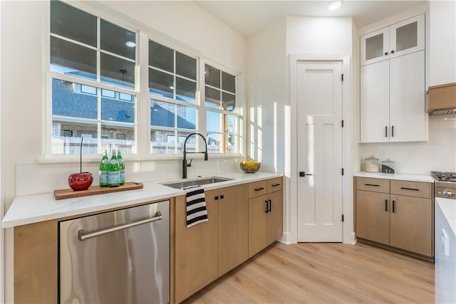 kitchen with sink, tasteful backsplash, light stone counters, light hardwood / wood-style flooring, and stainless steel dishwasher