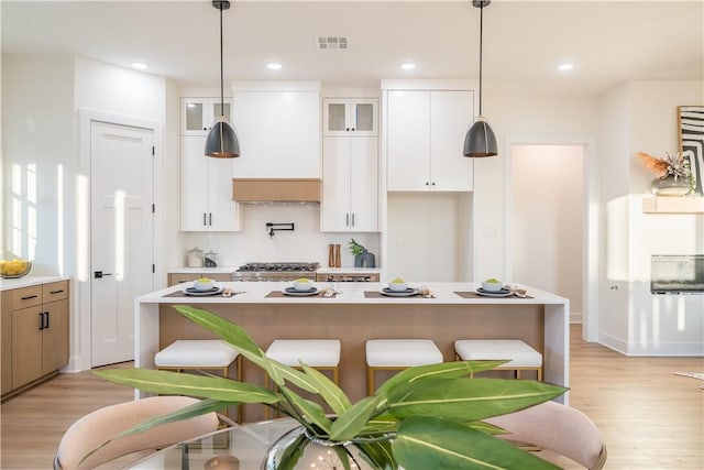 kitchen with white cabinets, custom range hood, light wood-type flooring, and hanging light fixtures