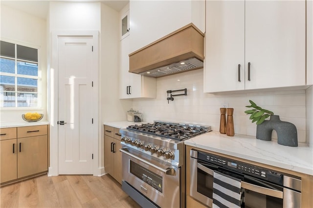 kitchen with stainless steel appliances, light stone counters, backsplash, light hardwood / wood-style floors, and custom exhaust hood