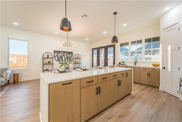 kitchen featuring a healthy amount of sunlight, light wood-type flooring, a kitchen island with sink, and light brown cabinets