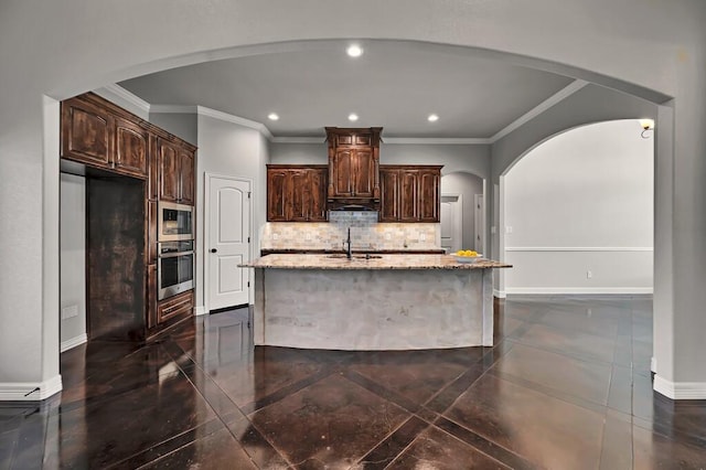 kitchen with backsplash, a kitchen island with sink, ornamental molding, dark brown cabinets, and stainless steel appliances